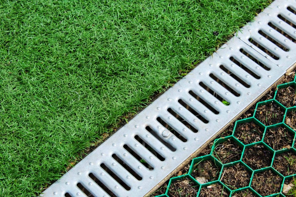 Thick green grass trimmed cleanly along a metal drainage grate